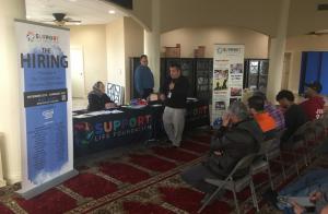 "The Hiring" Vertical banner frames a room of people attending a job fair