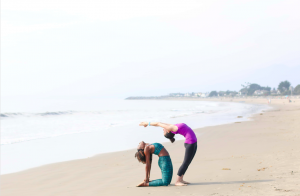 Two women practicing yoga on the beach