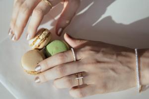 Hands wearing Joie de Viv sustainable fine jewelry gold and diamond rings holding green and brown macaroons.
