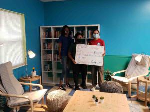 Young woman presenting an $800 donation check to representatives from the Quigley House shelter