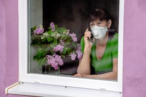 A sad lady wearing a face mask looks out of her window