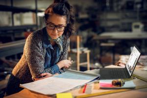 Woman working in home office, looking at complex product drawings while working remotely