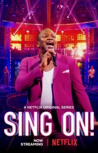 TV Host Tituss Burgess stands on stage with the Sing On Logo!
