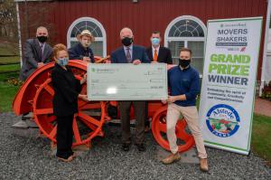 Photo of check presentation, six people stand by an old orange tractor. Three people in front row are holding a large check.