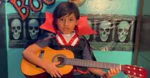 6 year old Jacob Marin plays the guitar in his vampire costume on his virtual stage.