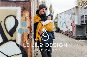Vater trägt Baby in senfgelbem Babytragetuch von LE Lilo Design in urbaner Umgebung.