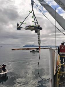 A cabled underwater listening frame being lowered off a vessel by crane into the water in Boundary Pass