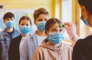 Teenage children in masks getting temperature checks for Covid in the classroom
