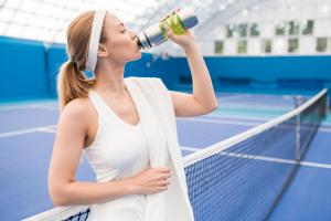 woman drinking water on tennis court