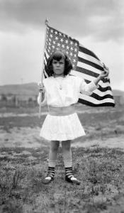 Photograph by Lora Webb Nichols of Ruth Winkelman, young girl holding an American flag, from a parade in Encampment, Wyoming, 1911