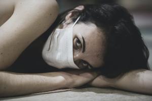 woman alone laying down in mask feeling social isolation due to COVID-19 lockdowns