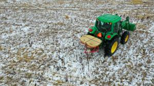 alt="Green tractor on snowy field spreads native seed mix containing seeds sourced from southern Illinois and Kentucky."