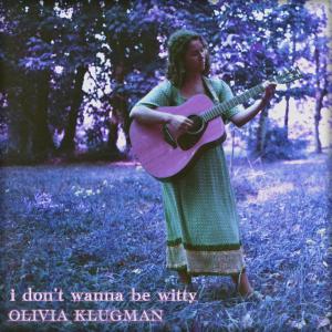 The cover art for Olivia Klugman's upcoming EP "i don't wanna be witty" Olivia playing a guitar in an open field.