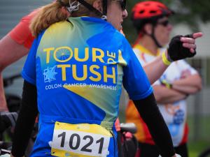 Image of the back of a bike rider wearing a Tour de Tush bike jersey.