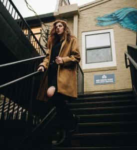 Zoe Hess in jeans and dark jaclet on a staitcase outside