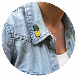 Photo of Pineapple Empowerment enamel pin symbolizing infertility awareness worn on a woman's jacket collar.