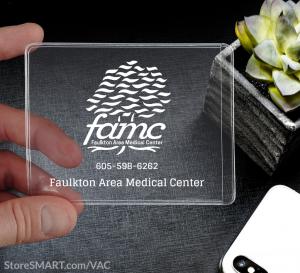 A hand holding a clear plastic pocket, 3-inch by 4-inch. The pocket has a logo of a tree with the letter f a m c under it with a phone number.