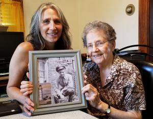 Daughter and Mother holding a framed photo of army soldier Tom Bolella in his WWII uniform.