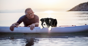 Senior man with a dog on a paddle board in the water.