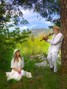 Dean serenades Dudley by the river, both dressed in white against the greenery.