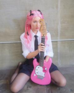Alex Slaone holding her guitar dressed in pink & black.