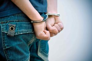 Child in blue jeans, arms handcuffed behind his back.