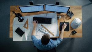 A male worker in an office, sat at a desk using software to produce a technical drawing