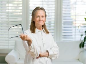 Blond-haired female in white shirt, in front of white window blinds