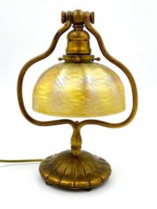 Tiffany Studios desk lamp with a gilt bronze harp form base with ribbed circular foot and a (cracked) Tiffany favrile glass damascened shade in gold ($4,612).