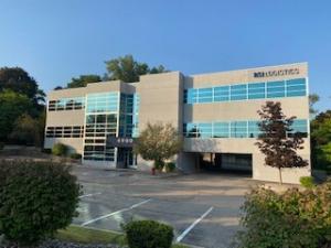 A grey building with blue windows and the words RSI Logistics at the top of the building; the building is surrounded by a parking lot and trees.