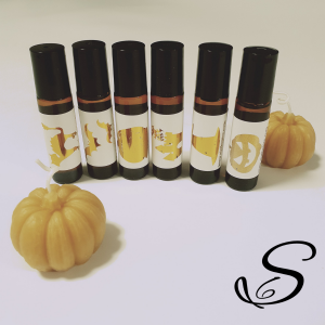 This photo shows six bottles of the perfumes standing upright right beside one another.  The bottles are turned so that the labels show the images.  The images are halloween characters such as a withc's hat, a haunted house, a cat with its back arched, a 