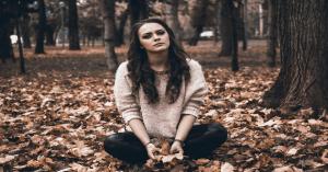 how to handle stress at work, Woman sits under the tree , the ground covered with leaves, looking stressful with deep thoughts