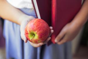 child in school uniform holding apple