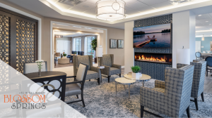 Elegant seating room with fireplace, TV, chairs and tables that residents can gather to socialize.