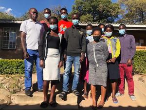 The first class of e-Learning students from the College of Nursing at Nkhoma in Malawi stand in front of a building, wearing masks.