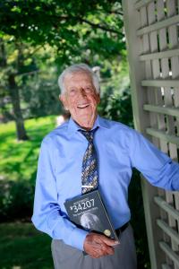 Joe Rubinstein holding a copy of the book about his life: Auschwitz #34207 The Joe Rubinstein Story (photo by Crystal Merrill 2019)