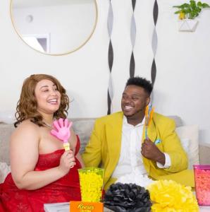 Models Crystal Renee and Lance Franklin II prepare for their Full Figured Industry Awards watch party. Both models are dressed in evening attire, sitting on a couch.