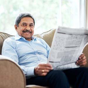 A man sits on a couch reading a newspaper and smiling toward the camera. Levine Benjamin Law Firm in Michigan helps people over 50 qualify for Social Security Disability benefits.