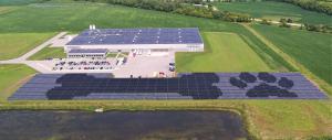 Artist rendering showing PetDine's expansive Harvard IL production facility, parking lot, neighboring fields and rows of solar panels with shaded shapes of a dog bone and pawprint on the panels.