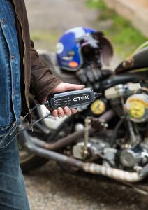 Man holding CTEK CT5 POWERSPORT charger near a motorcycle.