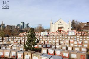 A large collection of boxes of food and clothing items gathered in front of INC Calgary congregation’s house of worship, with two ‘Aid To Humanity’ event banners on both sides of the chapel.