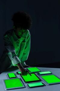 Ein Mann zeigt auf einen von mehreren Tablets und Smartphones auf einem Tisch. Ihre Displays leuchten grün.