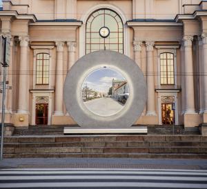 Video portal installation in front of a municipal building, showing another city on the screen