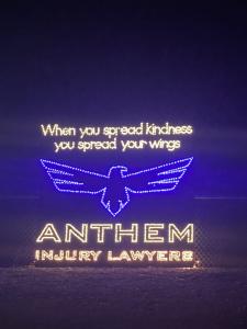 White and blue holidays lights that say "When you spread kindness you spread your wings" and the Anthem Injury Lawyers logo of an eagle.