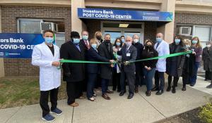 Photo shows ribbon cutting in front of the Investors Bank Post COVID-19 Care Center and includes doctors, healthcare professionals, medical center executives and leaders of a local commercial bank