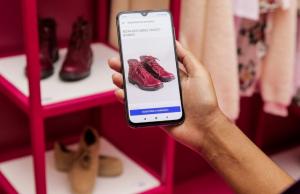 Un teléfono móvil con un catálogo de calzado en línea, revisando referencias y comentarios del producto al mismo tiempo que está en el comercio físico.