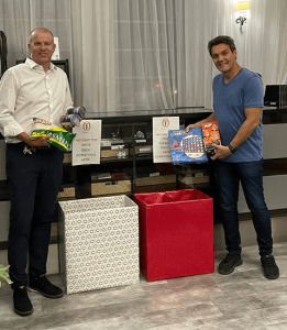 ALT="Hassan Jalali Bidgoli, Ocean Five hotelier standing on the right, holds two games to drop into a collection box for the Ocean Five Hotel holiday toy and food drive. On the left is Kevin McLaney, director of operations, holding foodstuffs to drop into