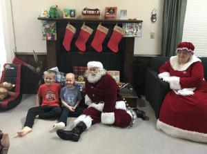 two boys, one with a cast, sitting with Santa and Mrs. Claus during an Edmarc Santa Run