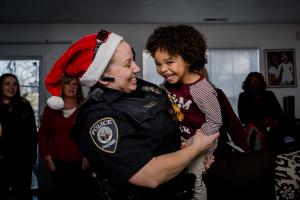 Police officer wearing a red Santa hat holds a child during an Edmarc Santa Run