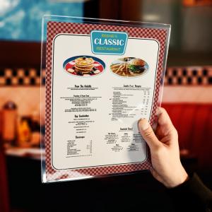 In a diner, a hand holds a menu. The menu is in a clear plastic protective cover.